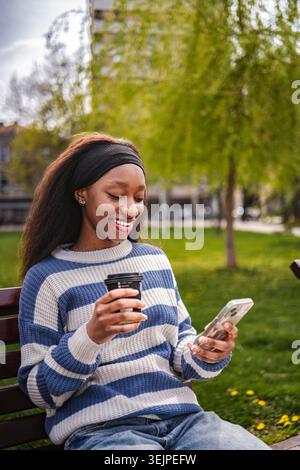 Frau genießt Kaffeepause im Park mit Smartphone Stockfoto