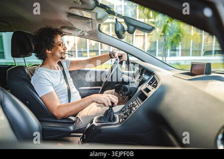 Mann mit lockigen Haaren, der Auto fährt und eine Zigarette raucht Stockfoto