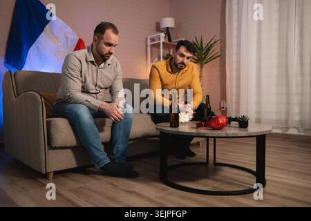 Freunde verbringen einen ruhigen Abend zu Hause mit Getränken und Snacks, während sie über das Leben in einem gemütlichen Wohnzimmer nachdenken Stockfoto