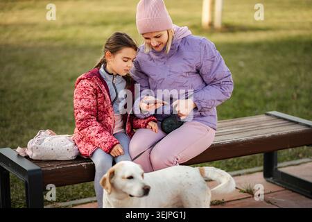 Mutter Tochter, die auf ein Smartphone schaut, das sich um einen Hund kümmert Stockfoto