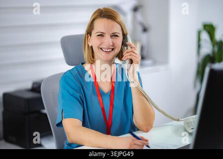 Krankenschwester am Telefon lächelnd in der Arztpraxis Stockfoto