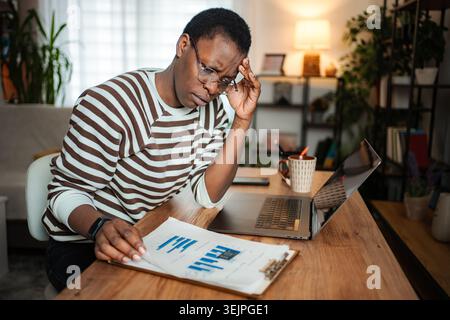 Gestresste junge Erwachsene Frau mit Kopfschmerzen bei der Arbeit von zu Hause aus Stockfoto