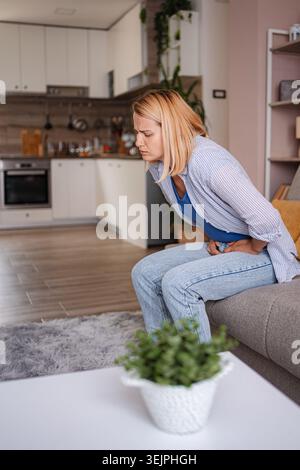 Frau, die Bauchschmerzen beim Sitzen auf dem Sofa im Wohnzimmer hat Stockfoto
