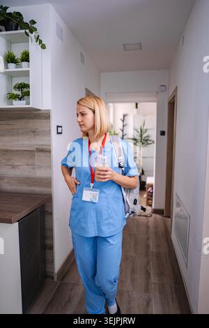 Krankenschwester, die im Krankenhausflur läuft und Eiskaffee hält Stockfoto