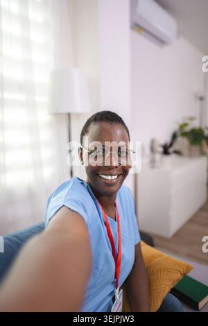 Lächelnde afroamerikanische Ärztin, die zu Hause Selfie macht Stockfoto