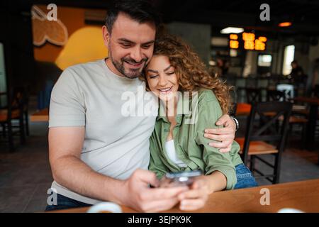 Ein Paar schaut sich das Smartphone an und lächelt im Café Stockfoto