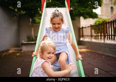 Zwei Kinder rutschen an einem sonnigen Tag mit Lachen herunter Stockfoto