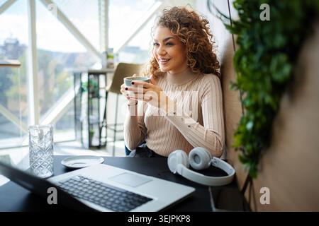 Glückliche junge Frau genießt Kaffee während der Fernarbeitszeit Stockfoto