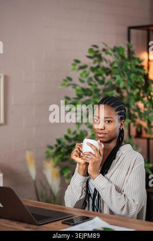 Junge Erwachsene Frau, die Kaffee trinkt und von zu Hause aus arbeitet Stockfoto