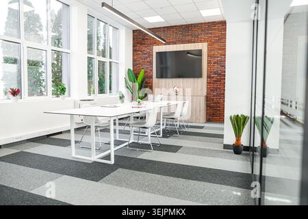 Ein Zimmer mit einem Tisch mit Stühlen und einem Flachbildfernseher an der Wand. Die Stühle sind ordentlich am Tisch platziert, in Richtung Stockfoto