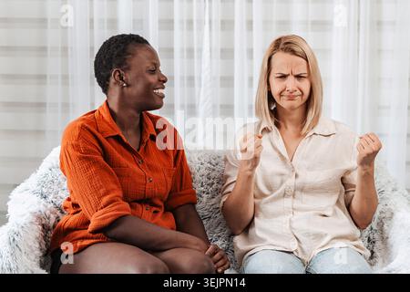 Frustrierte Frau, die ihren lächelnden Freund ansieht, während sie auf einem Sofa sitzt Stockfoto