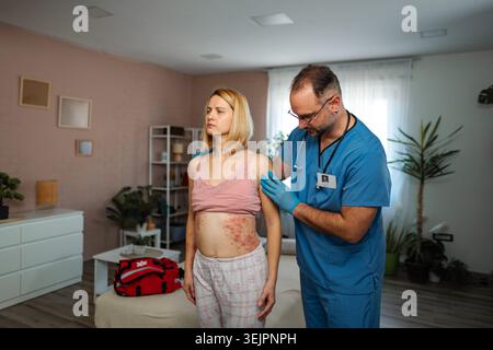 Der Arzt untersucht den Hautausschlag der weiblichen Patientin während des Hausbesuchs Stockfoto