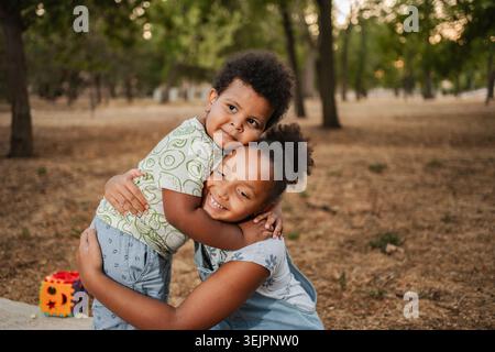 Zwei afroamerikanische Kinder, die sich in einem Park umarmen Stockfoto