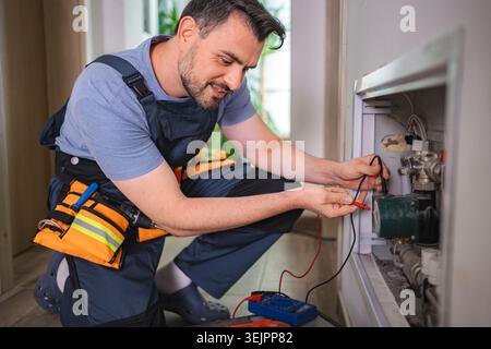 Elektriker, der die Spannung der Heizpumpe im Kesselraum misst Stockfoto