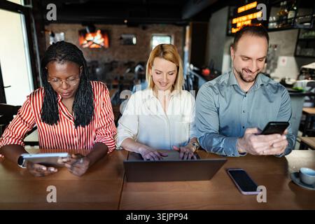 Verschiedene Kollegen arbeiten gemeinsam an digitalen Geräten im Café Stockfoto