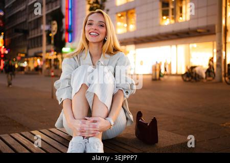 Glückliche junge Frau, die nachts in Wien auf der Bank sitzt Stockfoto