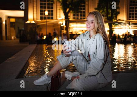 Junge Frau lächelt mit Smartphone am Wiener Brunnen Stockfoto