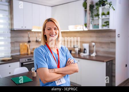 Porträt einer lächelnden Ärztin in blauer Uniform, die in der Küche steht Stockfoto
