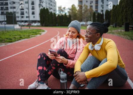 Zwei verschiedene Fitnessfreunde, die ihr Smartphone auf der Laufstrecke teilen Stockfoto