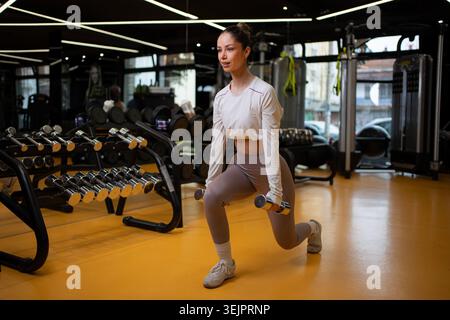 Eine junge Frau, die mit Kurzhanteln in einem Fitness-Studio trainiert Stockfoto