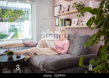 Frau, die sich zu Hause entspannt und gerne auf dem Sofa liest Stockfoto