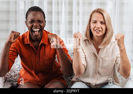 Zwei aufgeregte Freundinnen, die anfeuern und Sport im fernsehen gucken Stockfoto
