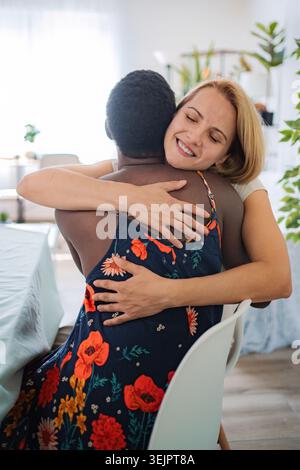 Zwei glückliche, multiethnische Freunde umarmen sich zu Hause Stockfoto
