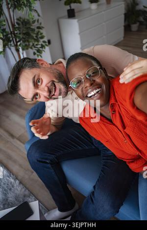 Glückliches Paar macht ein Selfie, während es zu Hause auf der Couch sitzt Stockfoto