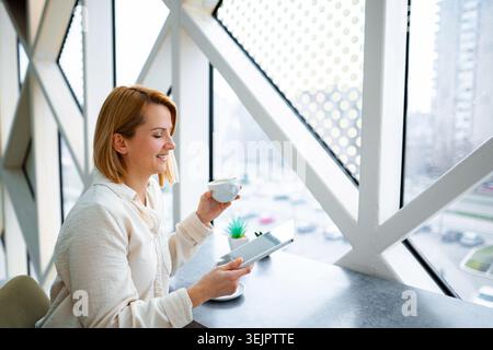 Frau genießt Kaffee mit einem digitalen Tablet im Café Stockfoto