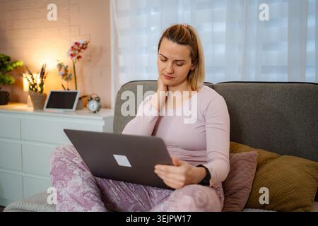 Frau, die am Laptop arbeitet, hat Nackenschmerzen im Bett Stockfoto