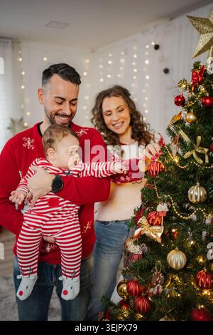 Familie mit Baby, die den Weihnachtsbaum für die Winterferien dekoriert Stockfoto