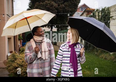 Verschiedene Freundinnen lächelnd halten Hände, die im Regen laufen Stockfoto