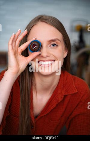 Eine junge Frau lächelt und hält einen Cupcake über dem Auge Stockfoto