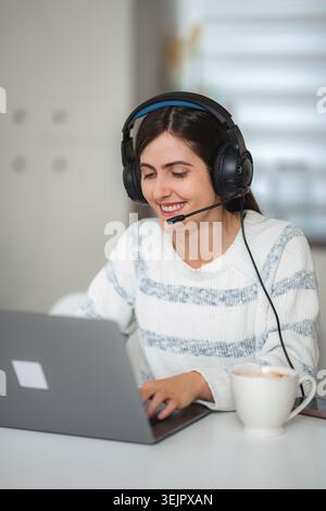 Frau mit Headset, die von zu Hause aus am Laptop arbeitet Stockfoto