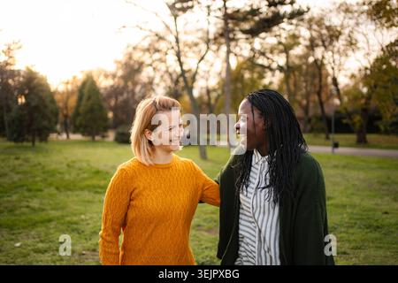 Verschiedene Freundinnen lächelnd reden im Park spazieren Stockfoto