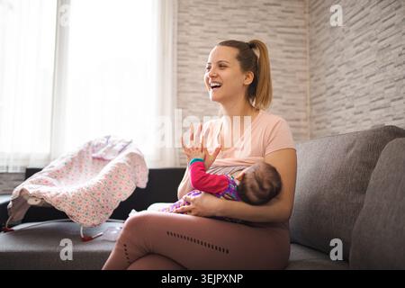 Mutter stillt ihr Baby tagsüber in einem gemütlichen Wohnzimmer Stockfoto
