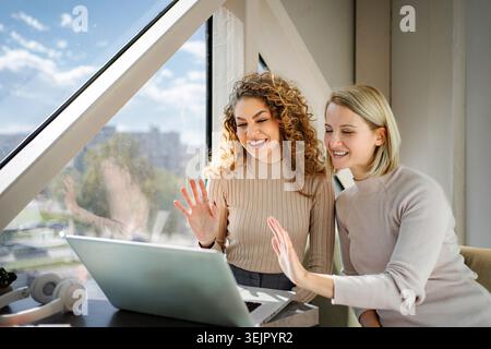 Glückliche Frauen, die während eines Online-Videoanrufs auf einem Laptop winken Stockfoto