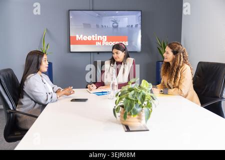 Verschiedene weibliche Arbeitskollegen in Geschäftskleidung, die Dokumente am Meeting-Tisch mit blauem Notizblock überprüfen. Sitzungssaal, Zusammenarbeit, Te Stockfoto