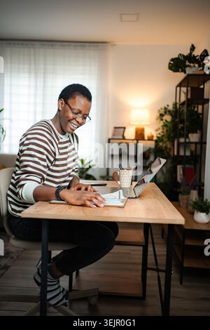 Frau, die von zu Hause aus arbeitet, lächelt beim Lesen von Dokumenten Stockfoto