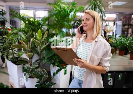 Florist macht sich Notizen und spricht am Telefon in einer Pflanzenwerkstatt Stockfoto