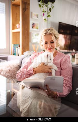Frau, die zu Hause Buch liest, mit weißer Katze Stockfoto