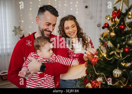 Familie, die Weihnachtsbaum mit glücklichem Baby zu Hause dekoriert Stockfoto