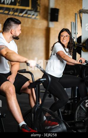 Ein Paar lächelt beim Training auf Air Bikes im Fitnessstudio Stockfoto