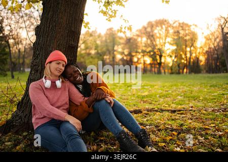 Verschiedene Freundinnen, die sich unter Bäumen im Herbstpark entspannen Stockfoto