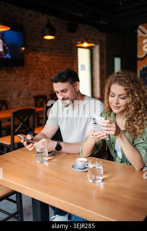 Junges Paar, das Smartphones benutzt, während er Kaffee im Café trinkt Stockfoto
