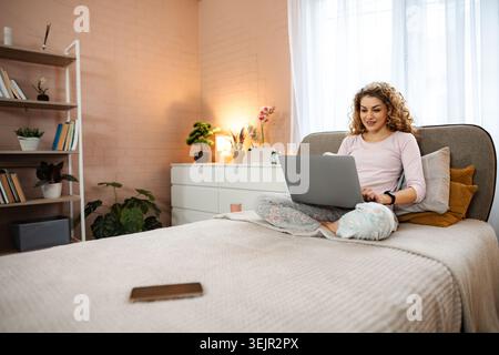 Frau, die von zu Hause aus mit Laptop im Bett arbeitet Stockfoto