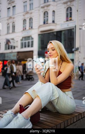 Junge Frau mit Smartphone, die in Wien auf der Bank sitzt Stockfoto