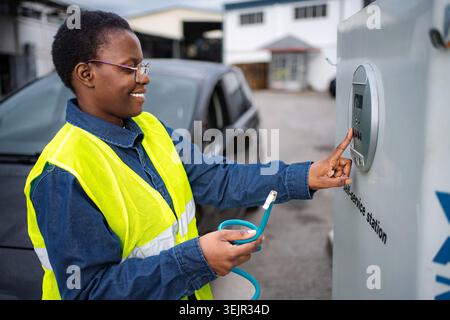 Frau, die Elektroauto an der Selbstbedienungsstation auflädt Stockfoto