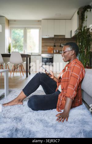 Junge Frau, die sich zu Hause entspannt und soziale Medien auf dem Smartphone durchsucht Stockfoto