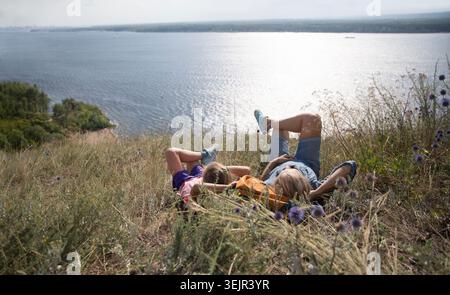 Glückliche Familienmutter und Tochter, die auf dem Gras am Berghang liegen und in die Ferne schauen Stockfoto